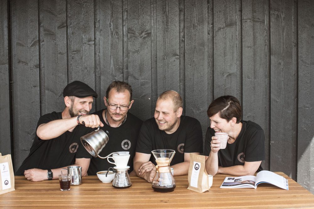 Fire kaffebrennere som smaker kaffe rundt et bord.